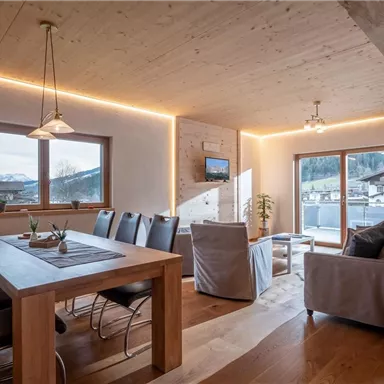 Ein modernes Wohn-Esszimmer mit Holztischen und -stühlen. Große Fenster bieten einen Blick auf die Berge und viel natürliches Licht.