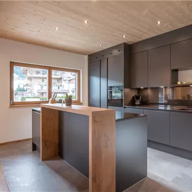 Moderne Küche mit Holz- und dunklen Elementen. Helle Räume und große Fenster schaffen eine einladende Atmosphäre.