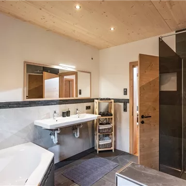 Ein modernes Badezimmer mit einer freistehenden Badewanne und einer begehbaren Dusche. Helle Wände und Holzverkleidungen sorgen für eine einladende Atmosphäre.