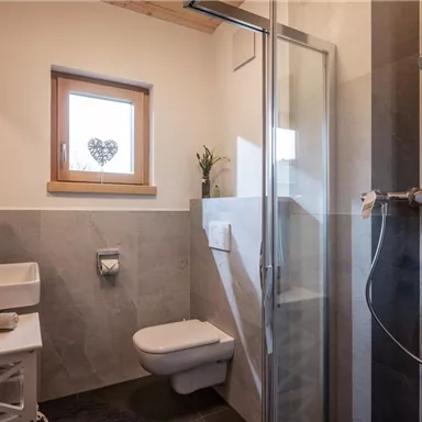 Ein modernes Badezimmer mit einer Dusche, einem Waschbecken und einem Fenster. Die Wände sind in neutralen Farben gehalten und es gibt eine Pflanze für einen Hauch von Grün.