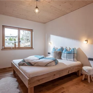 Ein gemütliches Schlafzimmer mit einem Holzbett und blauen Kissen. Natürliches Licht strömt durch das Fenster und schafft eine einladende Atmosphäre.