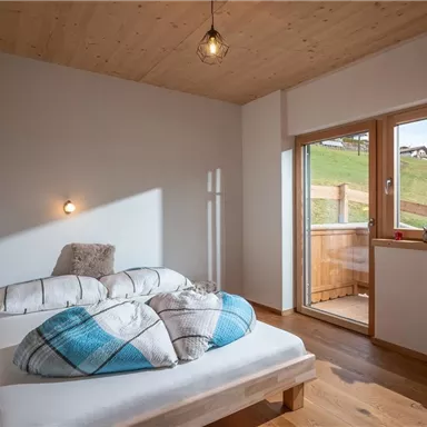 Ein gemütliches Schlafzimmer mit holzverkleideten Wänden und einem großen Fenster. Die Bettwäsche ist gemustert, und der Raum hat eine entspannte Atmosphäre.