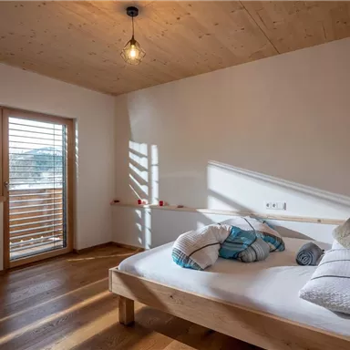 Ein gemütliches Schlafzimmer mit einem Holzbett und einer warmen Atmosphäre. Lichtstrahlen fallen durch das Fenster auf den gepflegten Boden.