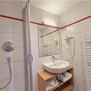 Ein modernes Badezimmer mit Dusche und Waschbecken. Die Wände sind gefliest und es gibt einen Handtuchwärmer.