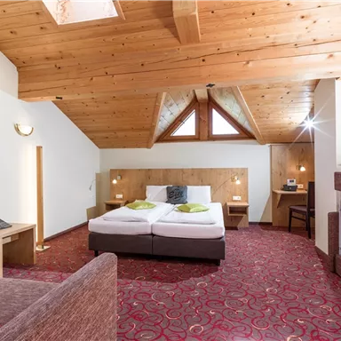 Ein gemütliches Hotelzimmer mit Holzbalkendecke und roten Teppich. Es bietet ein Doppelbett und eine zusätzliche Schlafgelegenheit.