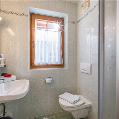 Ein modernes Badezimmer mit Dusche, Waschbecken und Toilette. Die Wände sind hell gefliest und ein Fenster sorgt für Tageslicht.