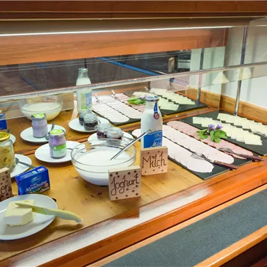 Ein reichhaltiges Frühstücksbuffet mit verschiedenen Käsesorten, Aufschnitt und Joghurt. Zusätzlich sind Butter und Milch auf dem Tisch platziert.