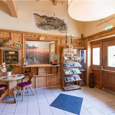 Ein gemütlicher Empfangsbereich mit Holzverkleidung und einem Tisch. An der Wand hängen Bilder und es gibt einen Informationsständer mit Broschüren.