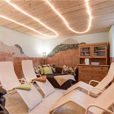 Ein gemütlicher Entspannungsraum mit Liegen und sanften Lichtern. Die Wände sind kreativ dekoriert, und der Raum wirkt einladend.