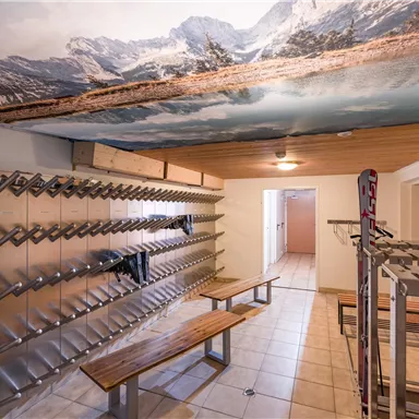 Ein sportlicher Raum mit Holzbänken und Metallschrank für Ausrüstung. An der Decke ist ein großes Bergmotiv zu sehen.