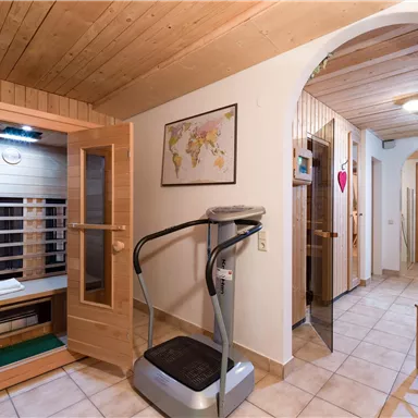 Ein moderner Wellnessbereich mit einer Sauna und einem Vibrationsgerät. Der Raum hat helle Fliesen und eine angenehme, einladende Atmosphäre.