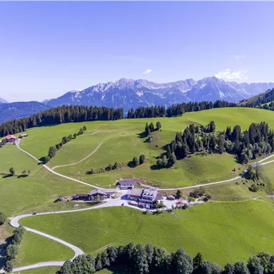 Eine malerische Landschaft mit grünen Wiesen und sanften Hügeln. Im Hintergrund sind majestätische Berge zu sehen.