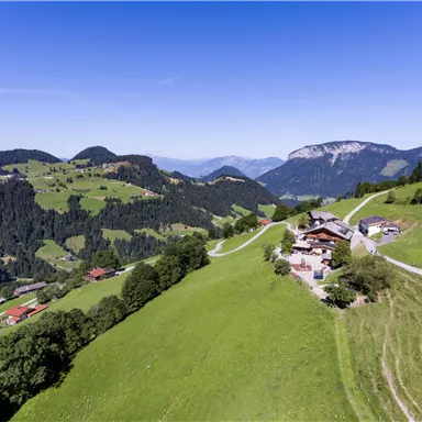 Eine wunderschöne Landschaft mit grünen Wiesen und sanften Hügeln. Im Hintergrund sind Berge und ein klarer Himmel zu sehen.