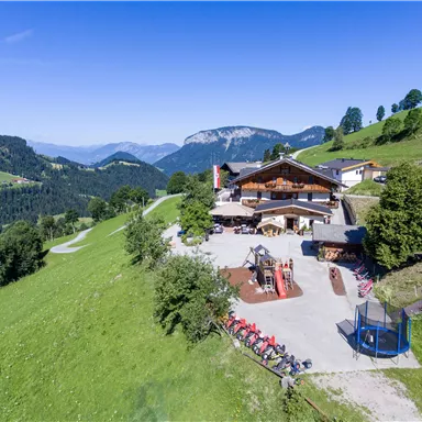Ein malerisches Landhaus auf einer grünen Wiese mit Blick auf die Berge. Der Außenbereich bietet Spielgelegenheiten für Kinder und einen schönen Ausblick.