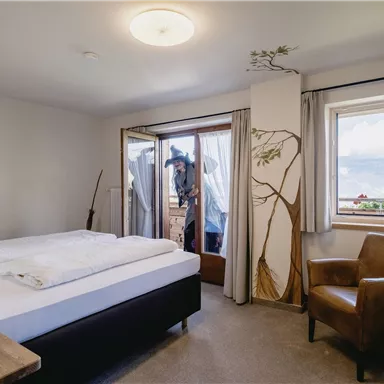 Ein modernes Schlafzimmer mit einem Doppelbett und einem gemütlichen Sessel. Große Fenster bieten einen Blick auf die Umgebung und es gibt eine stilvolle Wanddekoration.