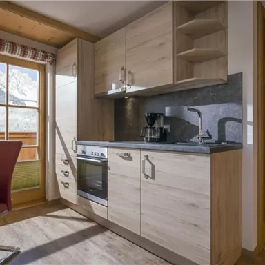 A modern kitchen unit with wooden cabinets and a window that offers a view of the mountains. The kitchen is well-equipped and brightly lit.