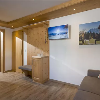 A cozy room with wooden paneling and a modern seating area. A television and a landscape painting are hanging on the wall.