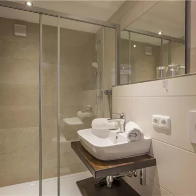 A modern bathroom with a shower and an elegant sink arrangement. The walls are brightly tiled, and there are fresh towels in soft colors.