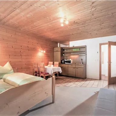 A cozy room with wooden walls and two beds. There is a small kitchenette and a dining table with chairs.
