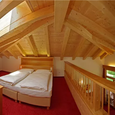 Ein helles und gemütliches Schlafzimmer mit Holzbalken und einem großen Fenster. Das Zimmer hat ein Doppelbett und eine offene, einladende Gestaltung.