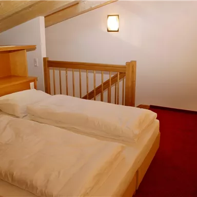 Ein helles Schlafzimmer mit zwei Einzelbetten und Holzdetails. Die Wände sind schlicht und die Atmosphäre ist gemütlich.