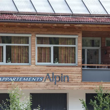 Eine moderne Holzfassade mit großen Fenstern. Der Schriftzug „APPARTEMENTS Alpin“ ist gut sichtbar.
