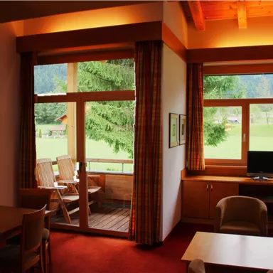 Ein gemütlicher Raum mit Holzdecke und großen Fenstern. Draußen ist eine grüne Landschaft sichtbar.