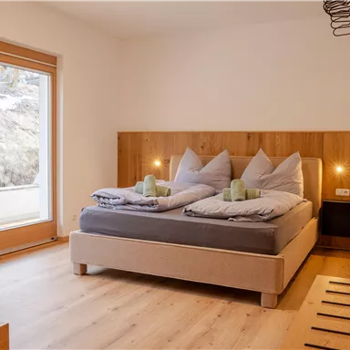 Ein modernes Schlafzimmer mit einem gemütlichen Doppelbett und zwei Kissen. Große Fenster bieten viel natürliches Licht und einen Blick auf die Landschaft.