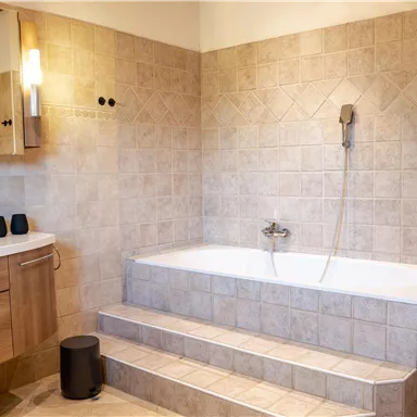 Ein modernes Badezimmer mit einer Badewanne und einer Dusche. Die Wände sind in neutralen Beige- und Brauntönen gefliest.