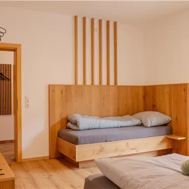 Ein modernes Zimmer mit Holzdetails und zwei Betten. Große Fenster sorgen für viel natürliches Licht.