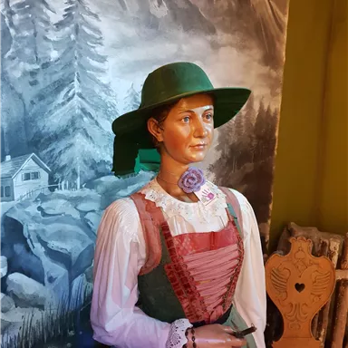 A lifelike figure in traditional attire with a green hat. In the background, a picturesque mountain landscape is visible.