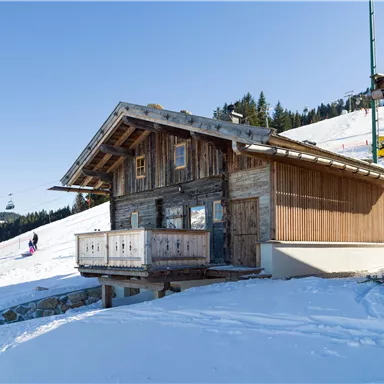 A charming wooden house in the midst of a snowy landscape. Ski slopes and trees can be seen in the background.