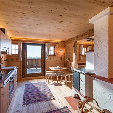 A cozy kitchen with wooden shelves and modern appliances. The room is brightly lit and has large windows overlooking the mountains.