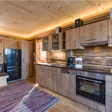 A modern wooden kitchen with appliances and a cozy seating area. The room has plenty of natural light and an inviting atmosphere.