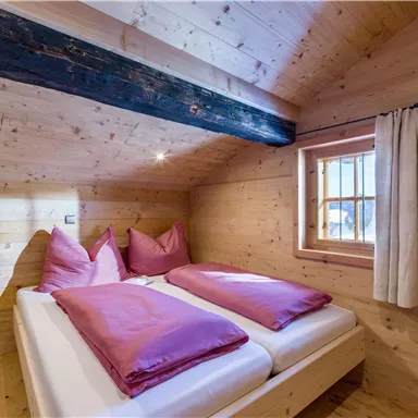 A cozy bedroom with wooden walls and a window. Two single beds with pink bedding are available.