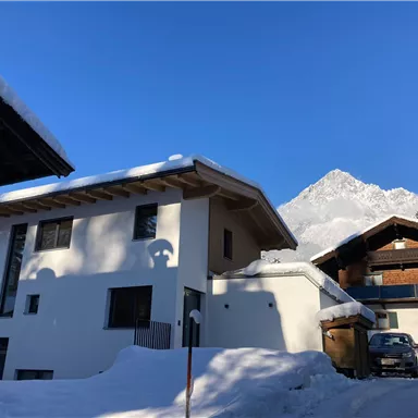 Eine ruhige Winterlandschaft mit schneebedeckten Häusern. Im Hintergrund ist ein majestätischer Berg unter klarem Himmel zu sehen.