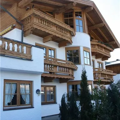 Ein schönes Holzhaus im traditionellen Stil mit Balkonen und großen Fenstern. Umgeben von grünen Sträuchern und einem klaren Himmel.