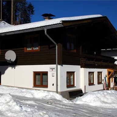 Ein gemütliches Haus im Schnee, umgeben von Bäumen. Der klare blaue Himmel ergänzt die winterliche Landschaft.