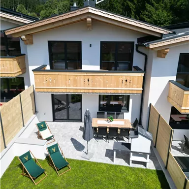 A modern chalet with a garden and terraces. On the terrace, there are lounge chairs and a dining table.