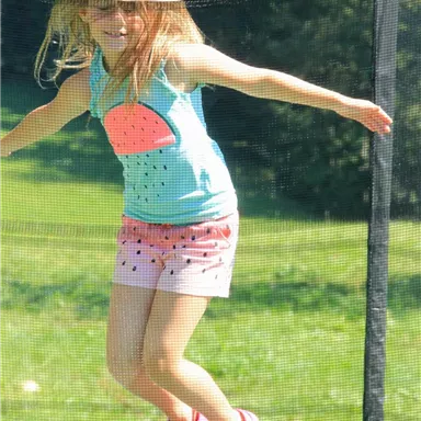 Ein kleines Mädchen springt fröhlich auf einem Trampolin. Sie trägt ein buntes Oberteil und Shorts, und die Sonne scheint.