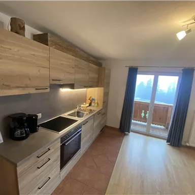 A modern kitchen with wooden cabinets and a kitchenette. It provides access to a balcony with a view.