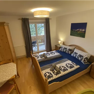 A cozy bedroom with two beds and wooden furniture. The room has a balcony and is brightly and friendly furnished.