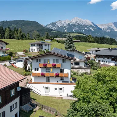 A picturesque village in the mountains with traditional houses and green meadows. In the background, majestic mountains and a blue sky can be seen.