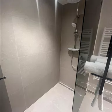 A modern shower with bright tiles and a glass partition. There is a rain shower and a towel warmer in the room.