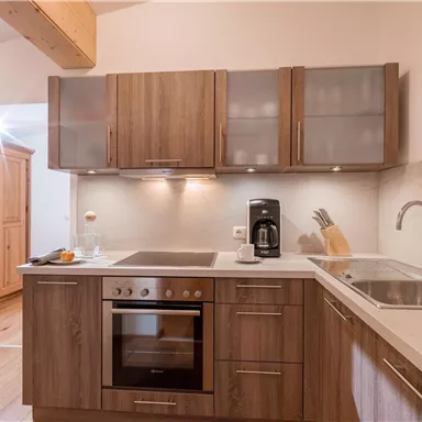 Eine moderne Küche mit Holzschränken und hellen Oberflächen. Ausgestattet mit einem Herd, einer Spüle und einer Kaffeemaschine.