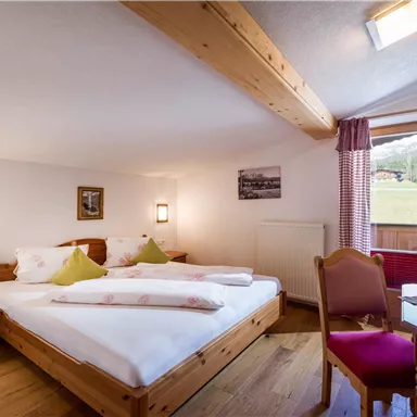 Ein gemütliches Schlafzimmer mit zwei Betten und Holzmöbeln. Ein Fenster bietet Blick auf die umliegende Natur.