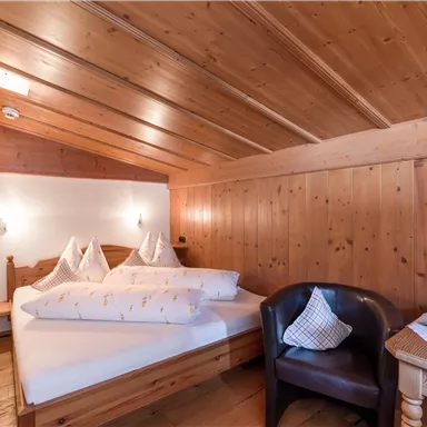 Ein gemütliches Schlafzimmer mit Holzverkleidung und zwei Betten. Es gibt einen Sessel und einen kleinen Tisch, die eine einladende Atmosphäre schaffen.