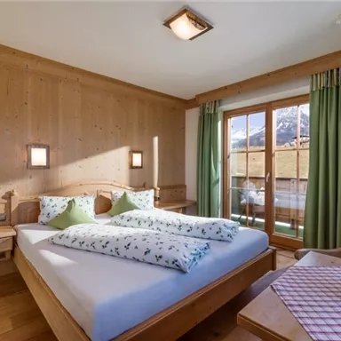 Ein gemütliches Schlafzimmer mit Holzwänden und großen Fenstern. Das Zimmer ist gut beleuchtet und hat ein Doppelbett mit Kissen in frischen Farben.