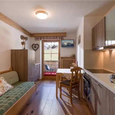 Eine gemütliche kleine Küche mit einem Essbereich und einer Schlafcouch. Große Fenster bieten einen Blick ins Freie und lassen viel Licht herein.