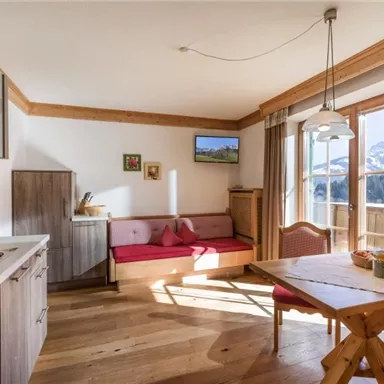 Eine gemütliche Küche mit einem Esstisch und einer Sitzgelegenheit. Große Fenster bieten einen Blick auf die Berge und lassen viel Licht hereinfällen.